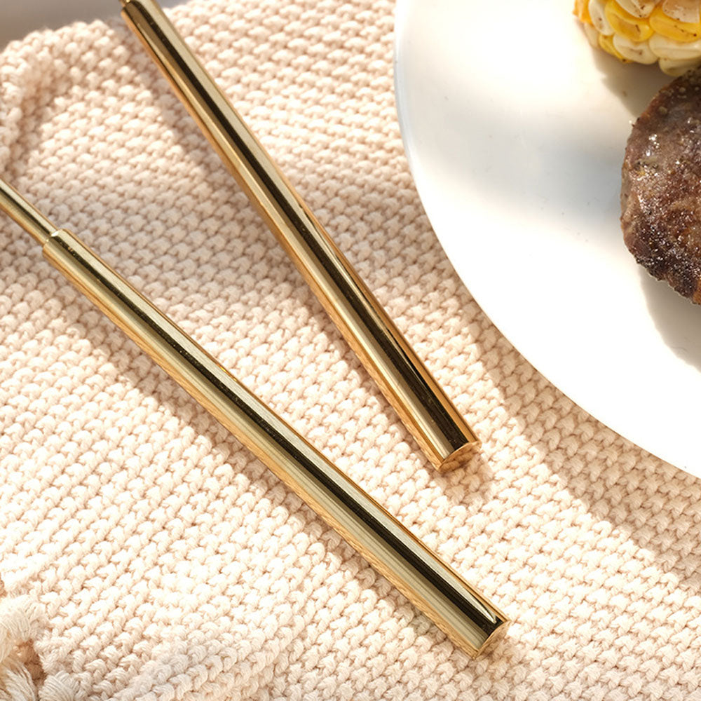 Two gold straws on a textured beige surface with a blurred background