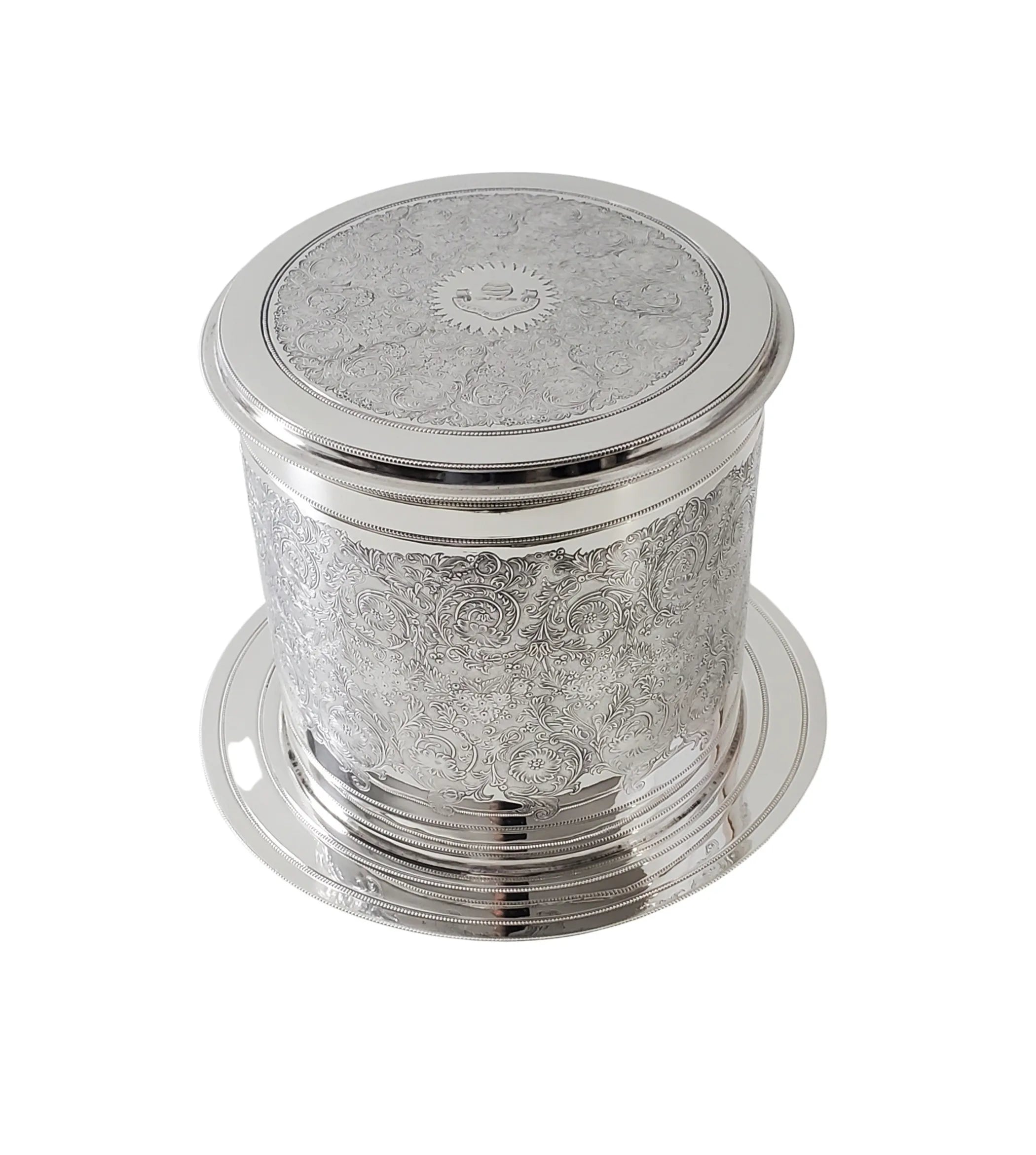 A round, silver-plated antique biscuit box with engraved floral patterns and a lid, against a white background.