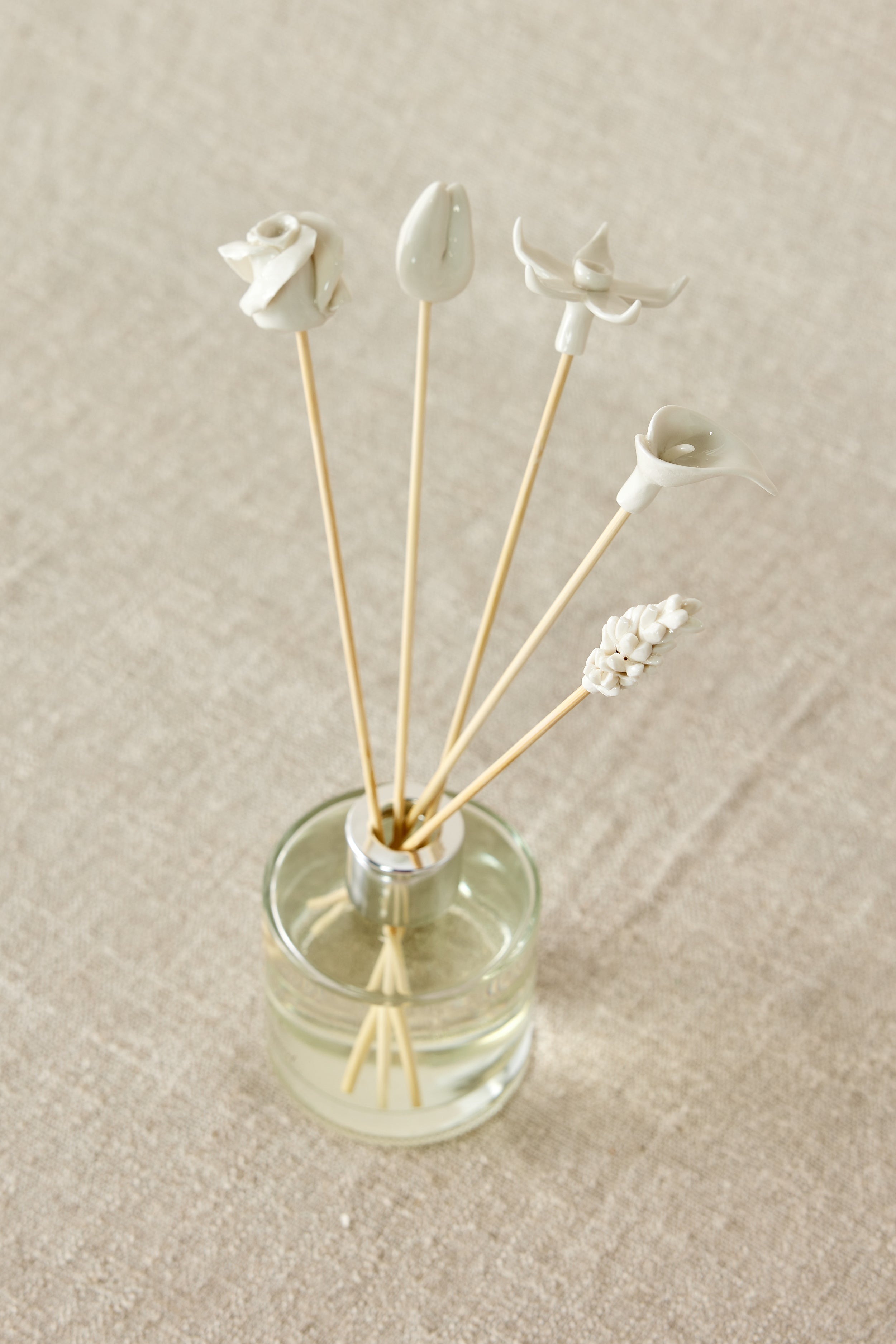 Clear glass diffuser bottle with wooden sticks and decorative elements on a beige fabric background