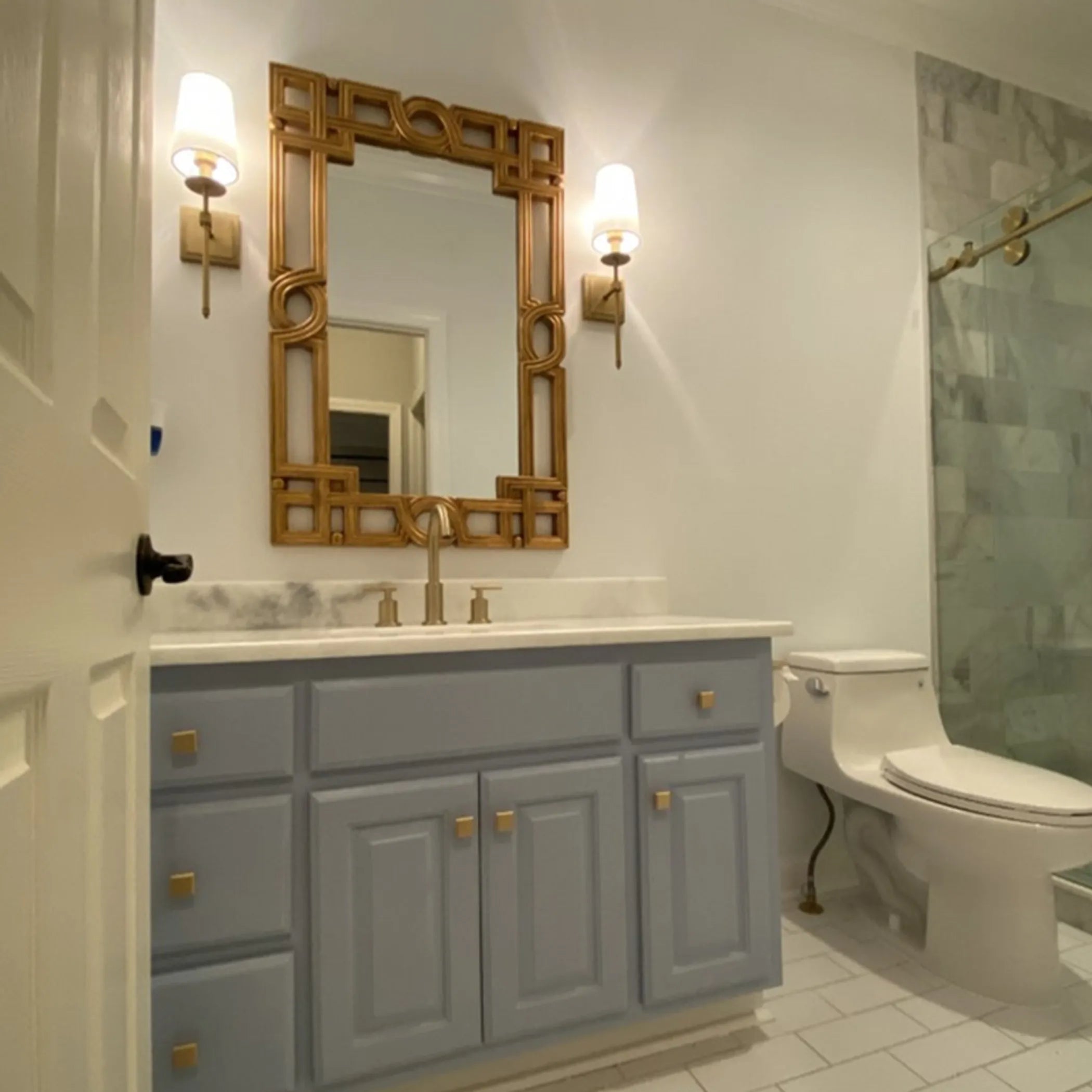 Bathroom with gray vanity, Artemis Antique Gold Openwork Frame Wall Mirror, and white toilet.