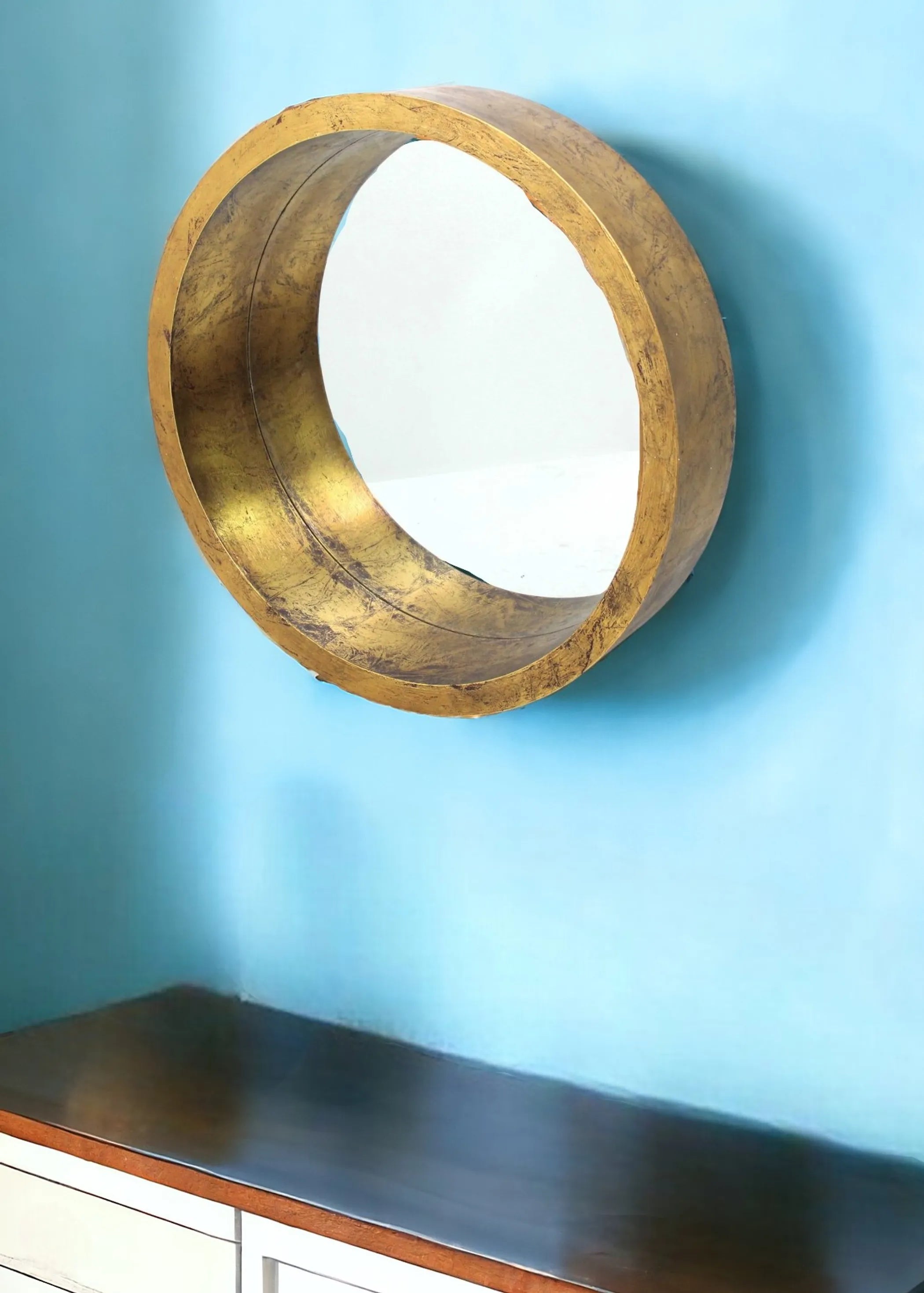 Round wooden mirror with gold finish on a blue wall