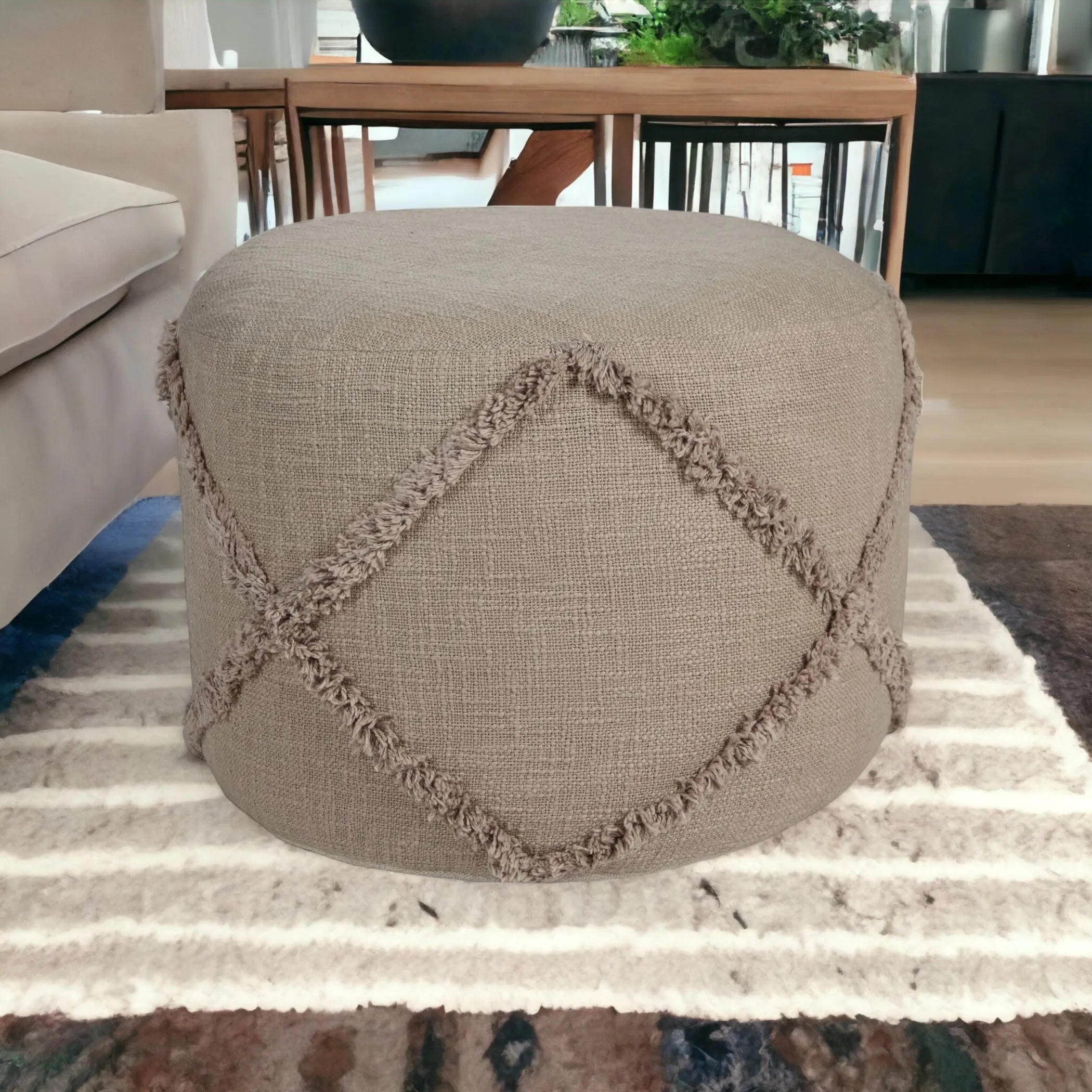 Round beige ottoman with decorative cross pattern on a striped rug