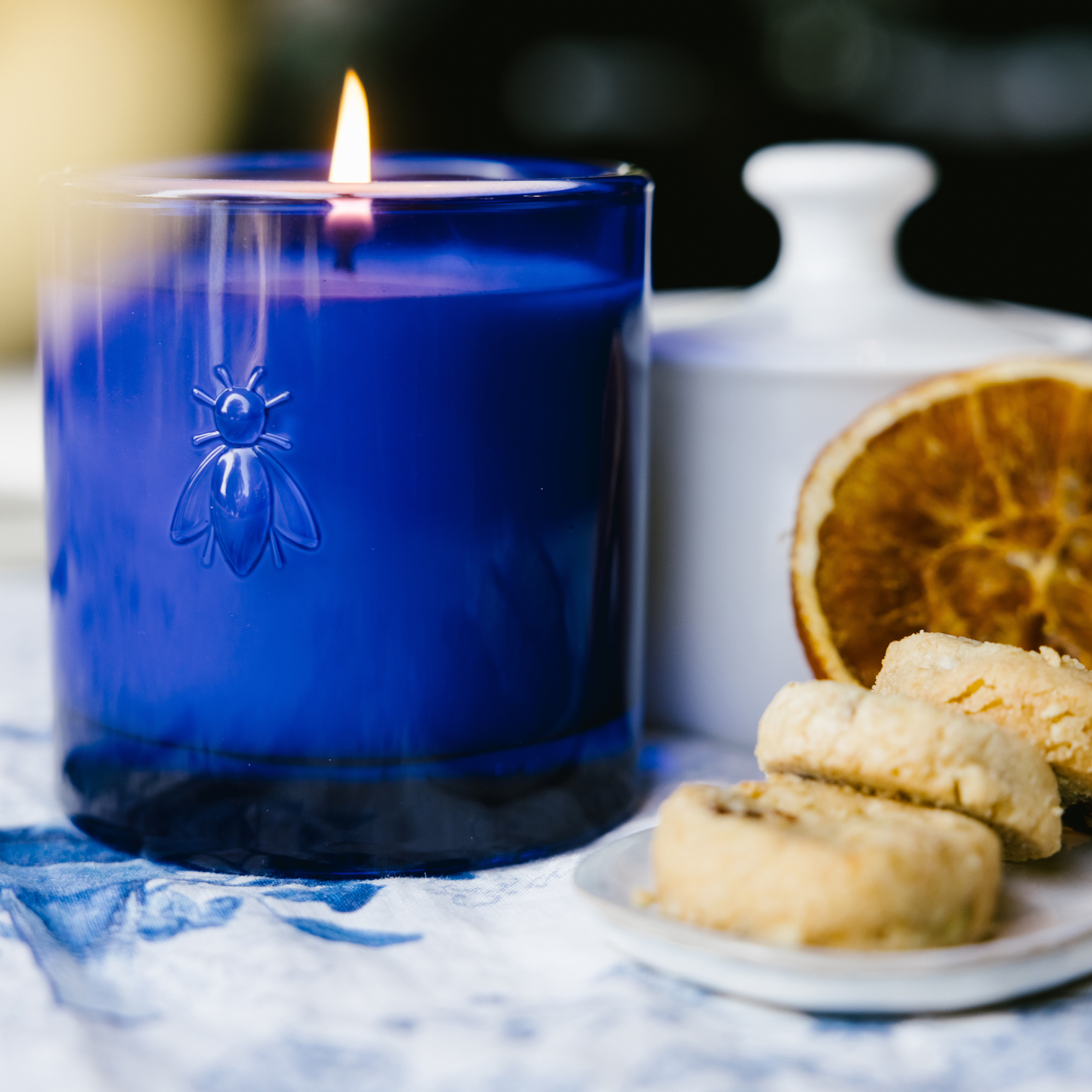 La Rochere Blue candle with a bee design next to cookies and dried oranges on a table.