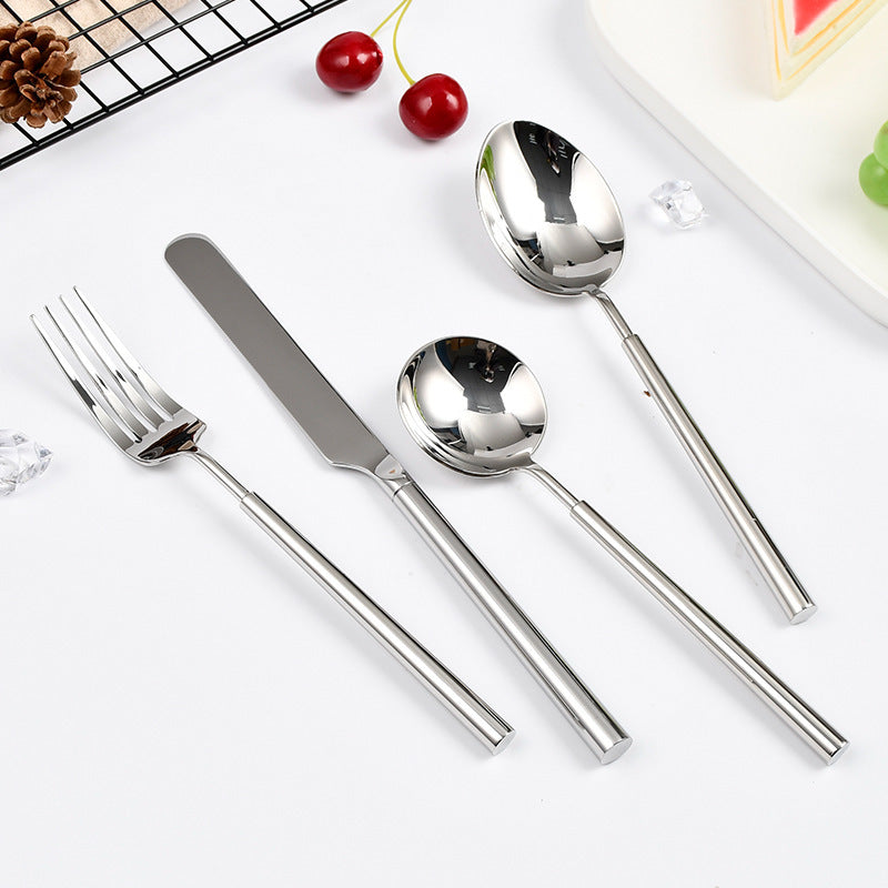Set of stainless steel cutlery including fork, knife, and two spoons on a white surface.