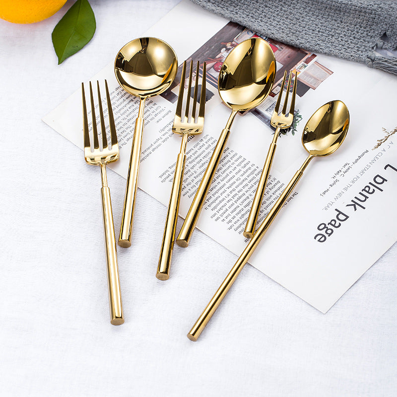 Set of gold cutlery including spoons and forks on a white surface with a magazine underneath.
