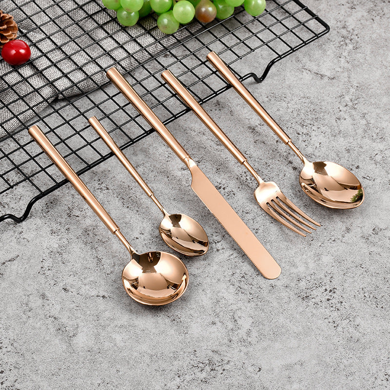 Set of rose gold cutlery including spoons and a fork on a gray surface with grapes in the background.