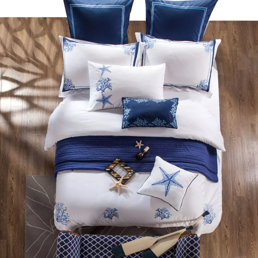 Nautical-themed bedding set with blue and white pillows and comforter on a wooden floor.