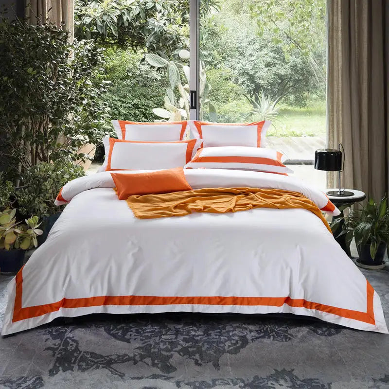 Bed with white and orange bedding in a room with large windows and greenery.