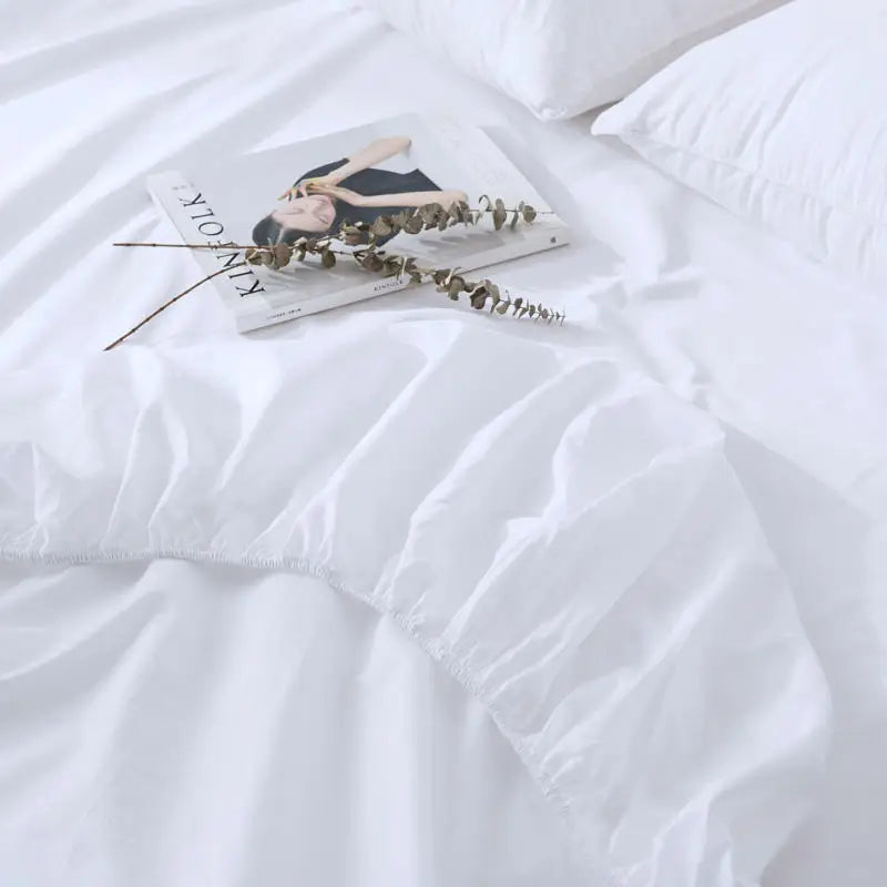 White comforter on a bed with a magazine and decorative branch on top