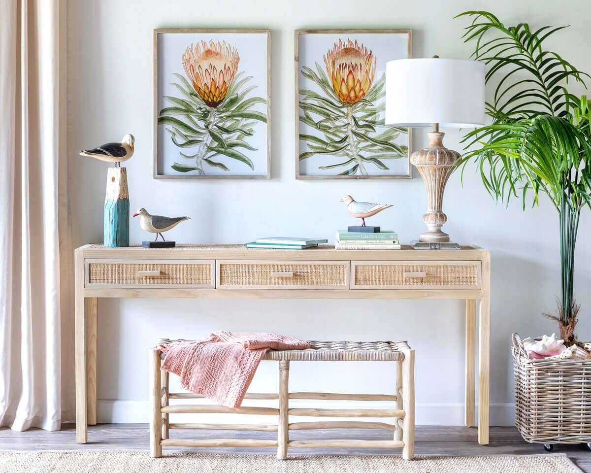 Light wooden console table with decorative items in a room with a lamp and plants.