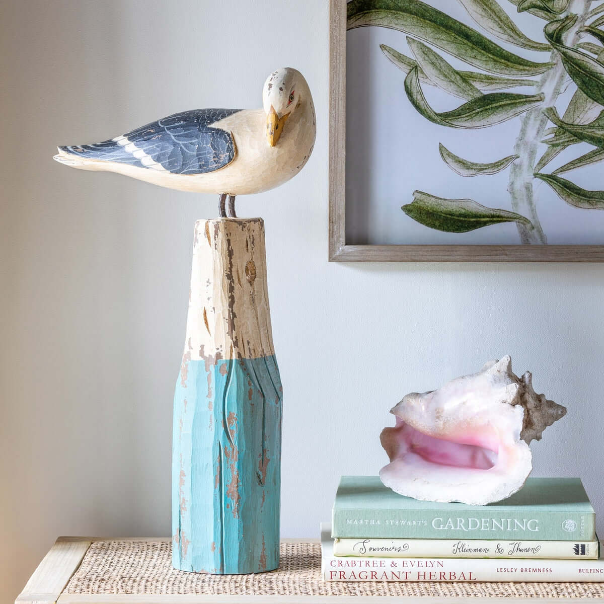 Decorative seagull on a wooden stand with a shell and book in the background.