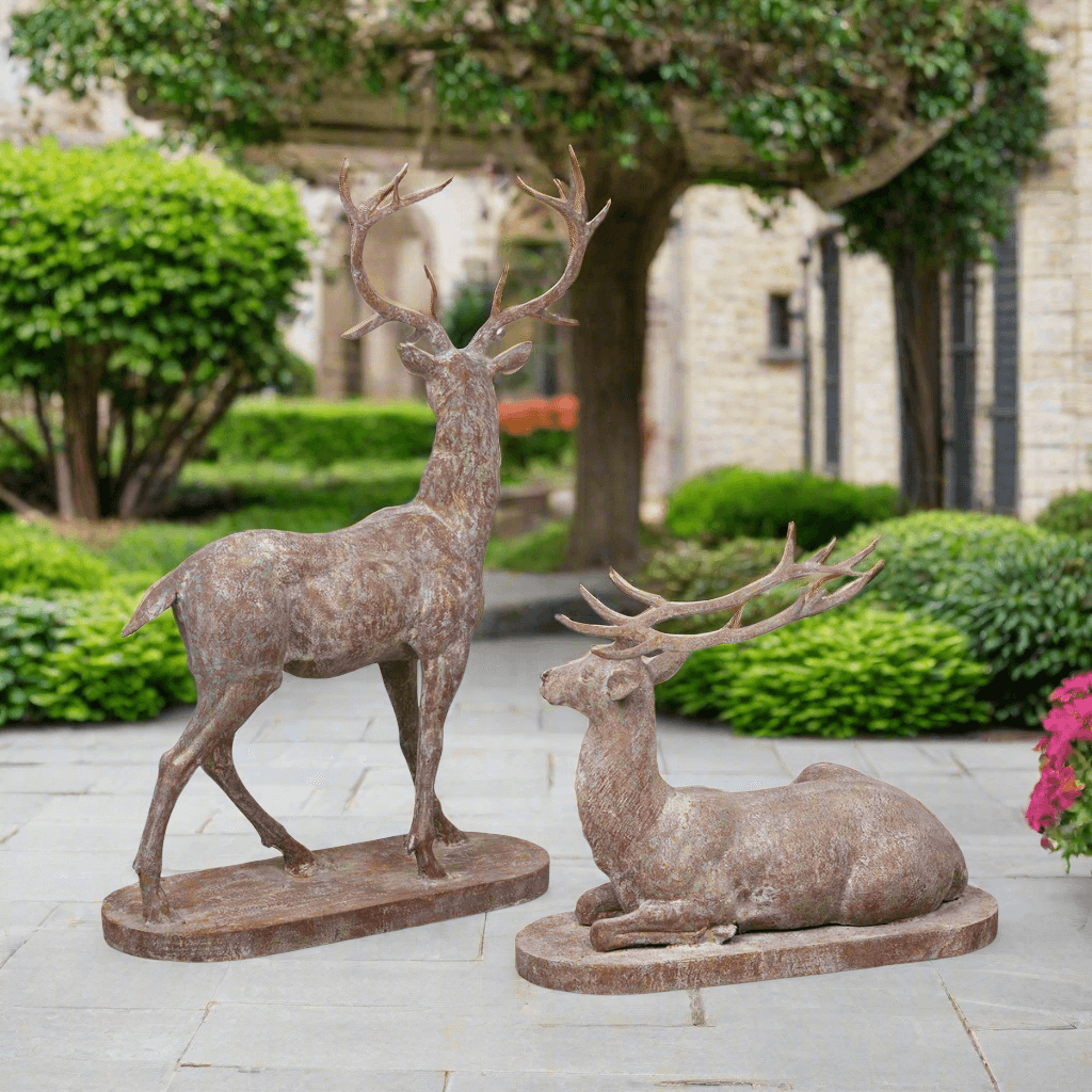 Two deer statues on a stone patio with a garden and building in the background
