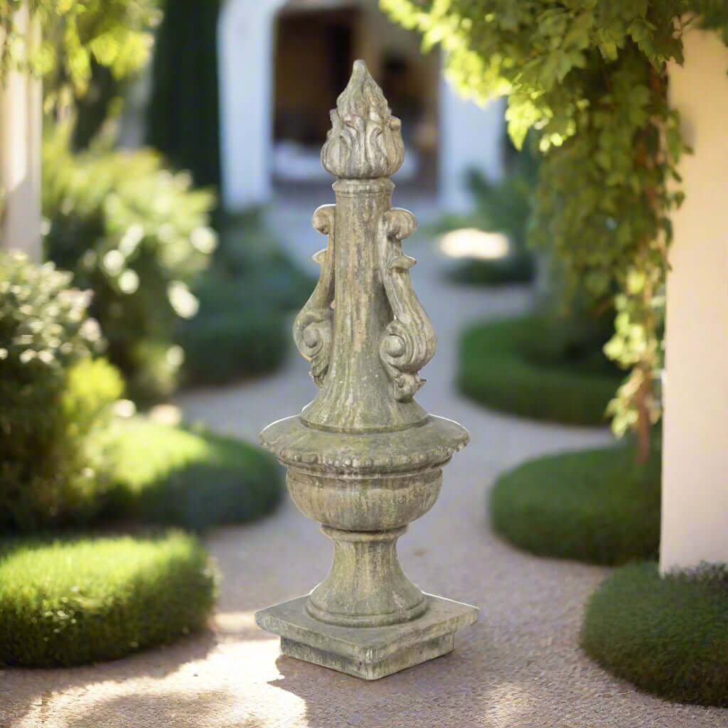 Decorative Grecian Garden Torch Statue in a garden setting with greenery and a building in the background