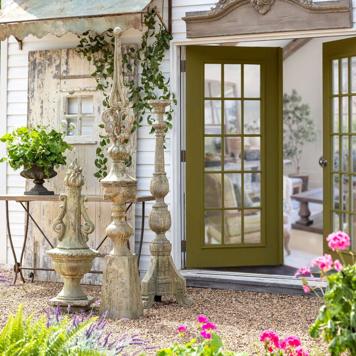 Decorative Grecian Garden Torch Statue with stone pillars, flowers, and a green door.