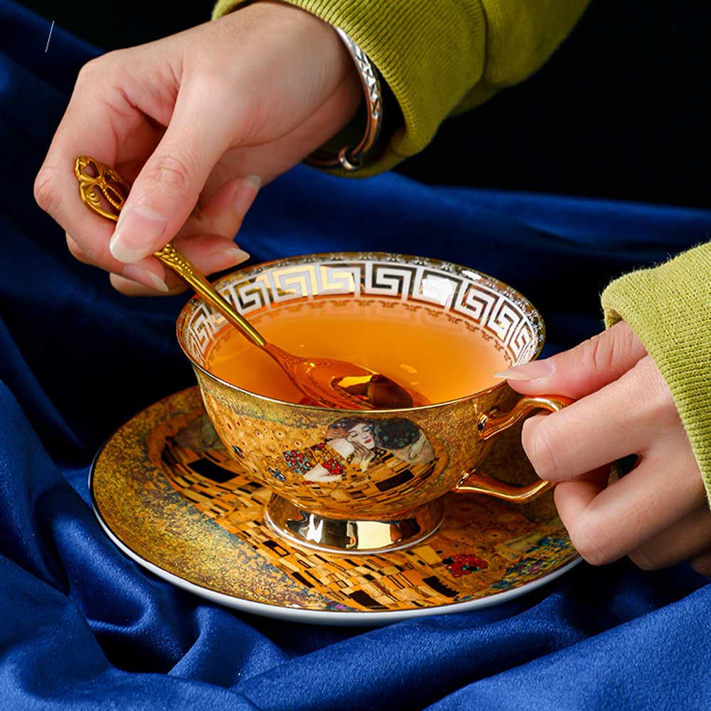 Person stirring tea in a decorative gold cup and saucer with a blue fabric background