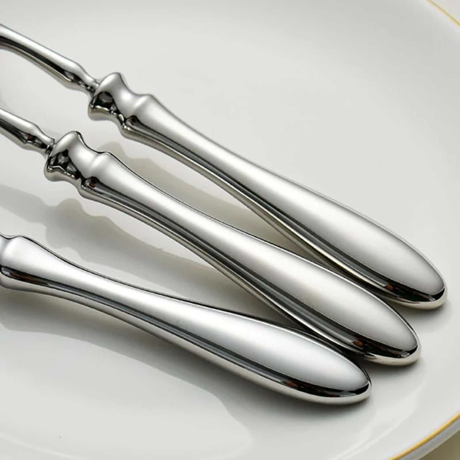 Close up of the handles of silver cutlery on a white plate with gold rim