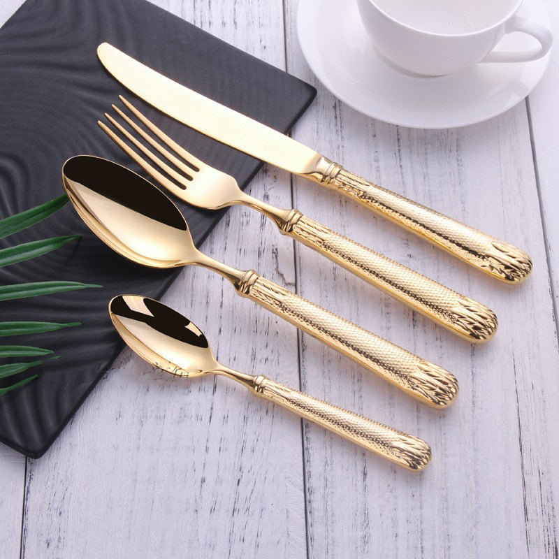 Set of gold cutlery on a wooden surface with a cup and saucer in the background.