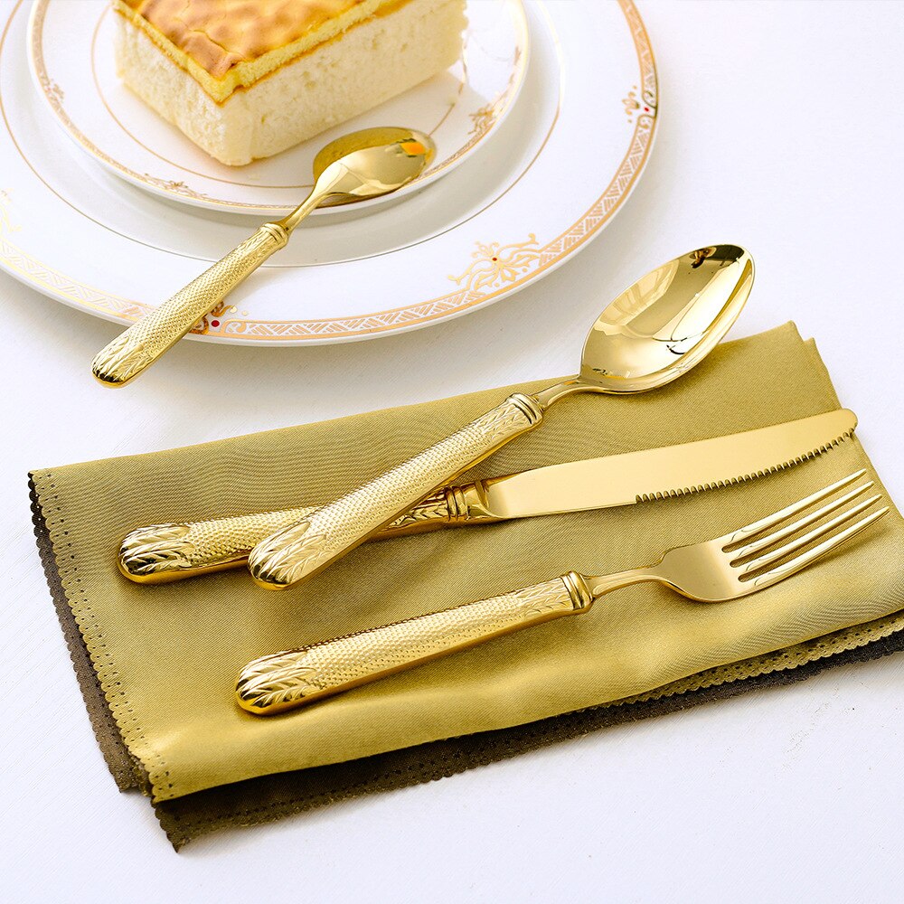 Gold cutlery set on a gold napkin with a dessert in the background