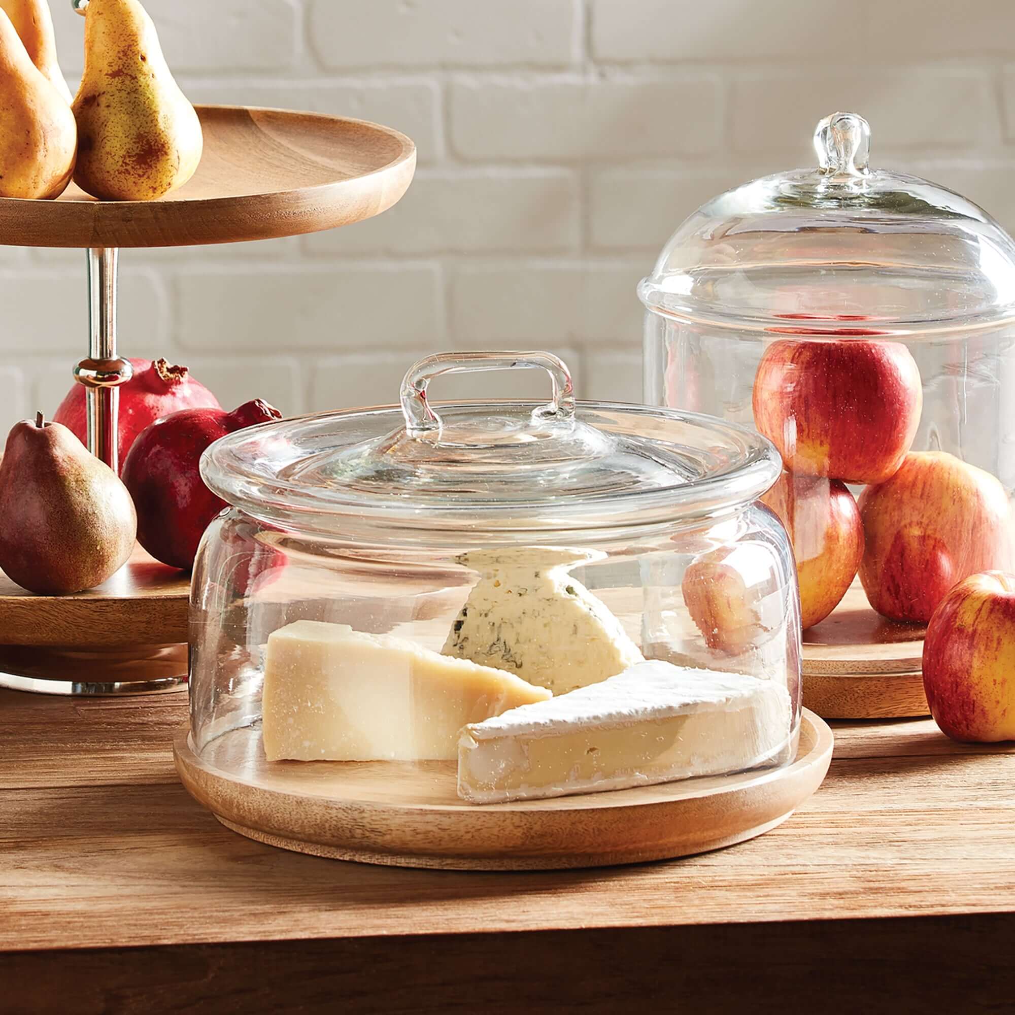 Glass cloche with wooden bases on a kitchen counter with fruits and pears.