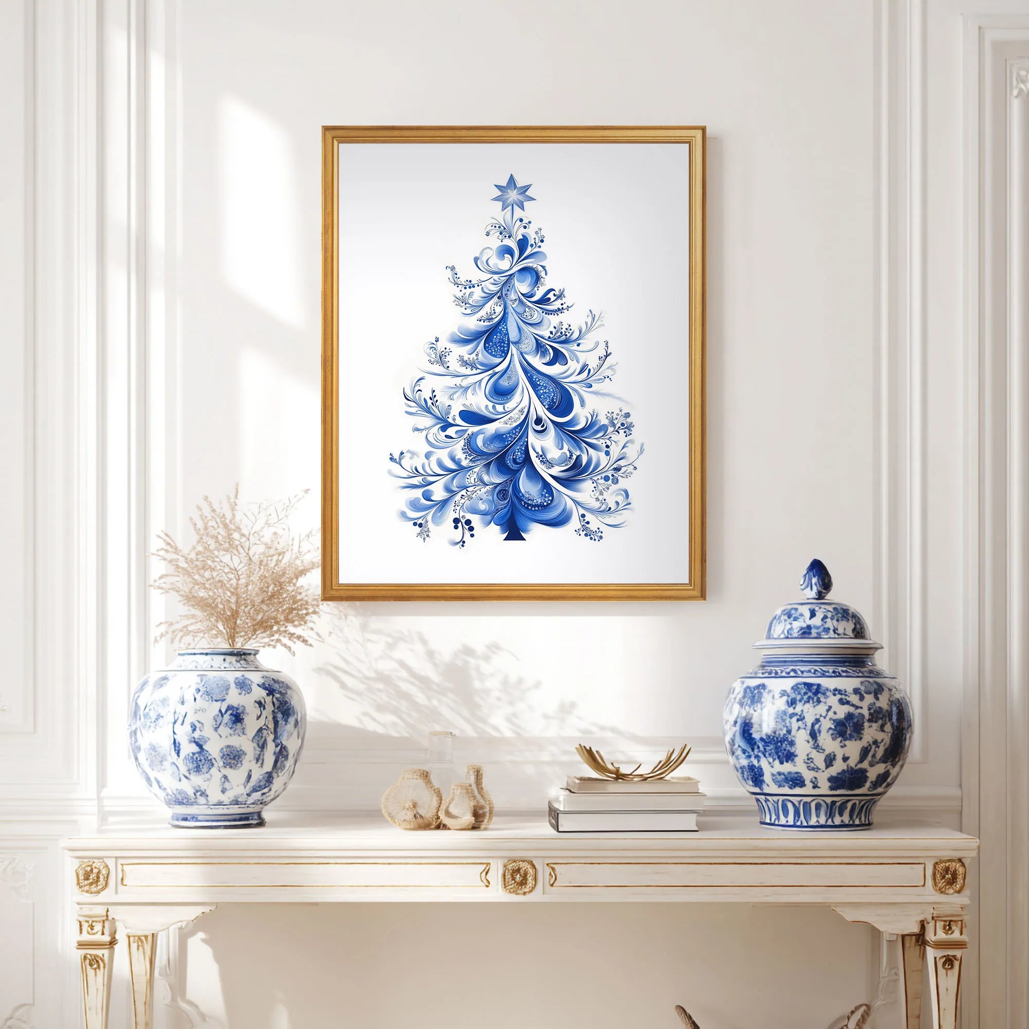 Framed blue Christmas tree artwork on a white wall above a decorative table with blue and white vases.