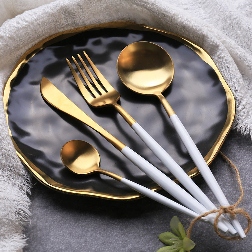 Set of gold and white cutlery on a black plate with a gray napkin.