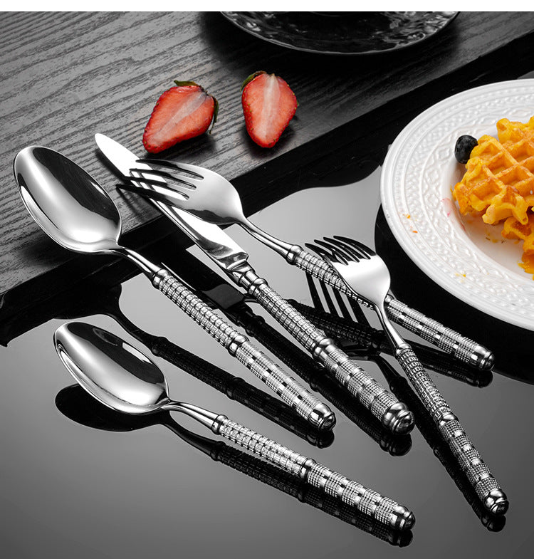 Set of silver cutlery with decorative handles on a wooden surface with strawberries and a plate of food.