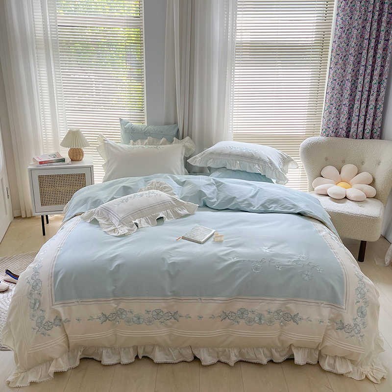 Light blue bedding set on a bed in a bright bedroom with curtains and a chair.