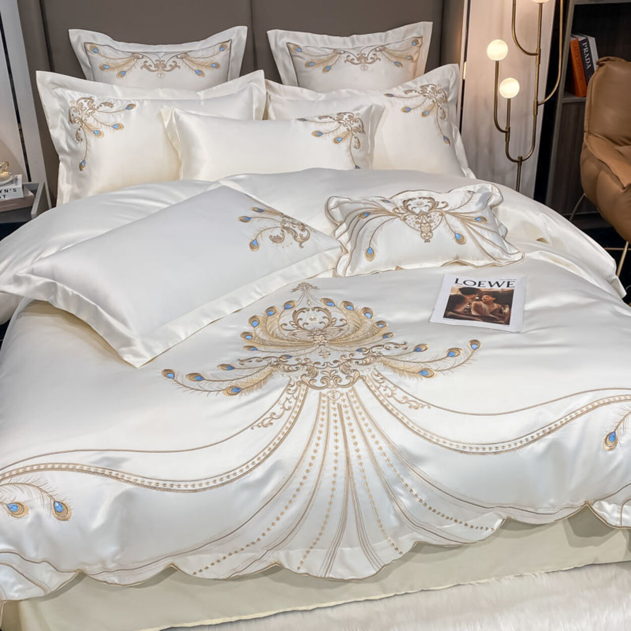Embroidered white bedding set with gold accents on a bed, featuring LOUISE branding.