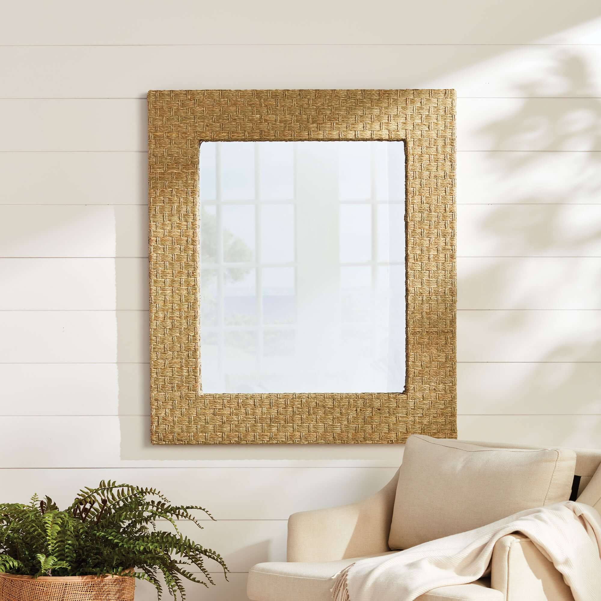 Woven mirror on a wall with a plant and sofa in the foreground