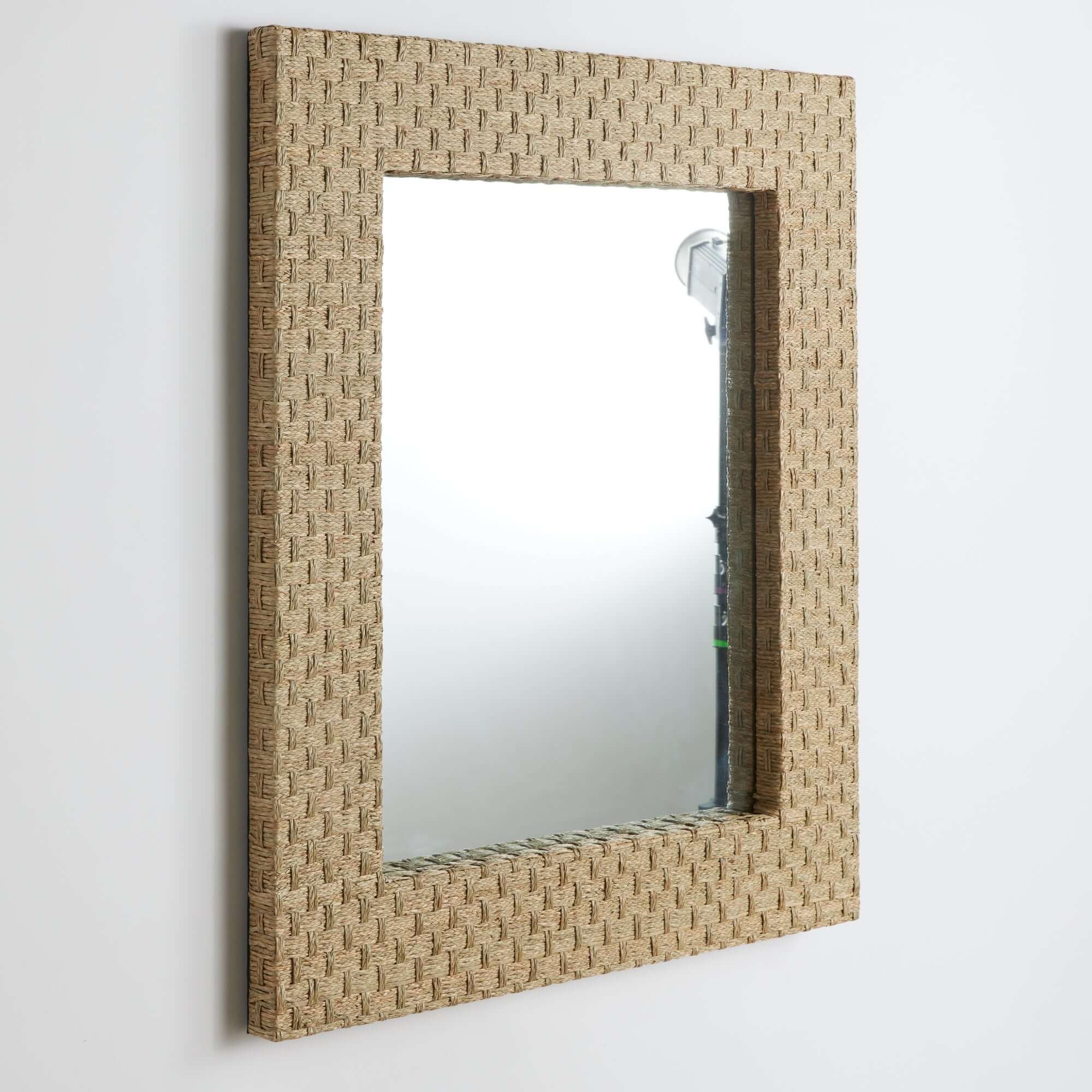 Rectangular mirror with woven beige frame on a white wall