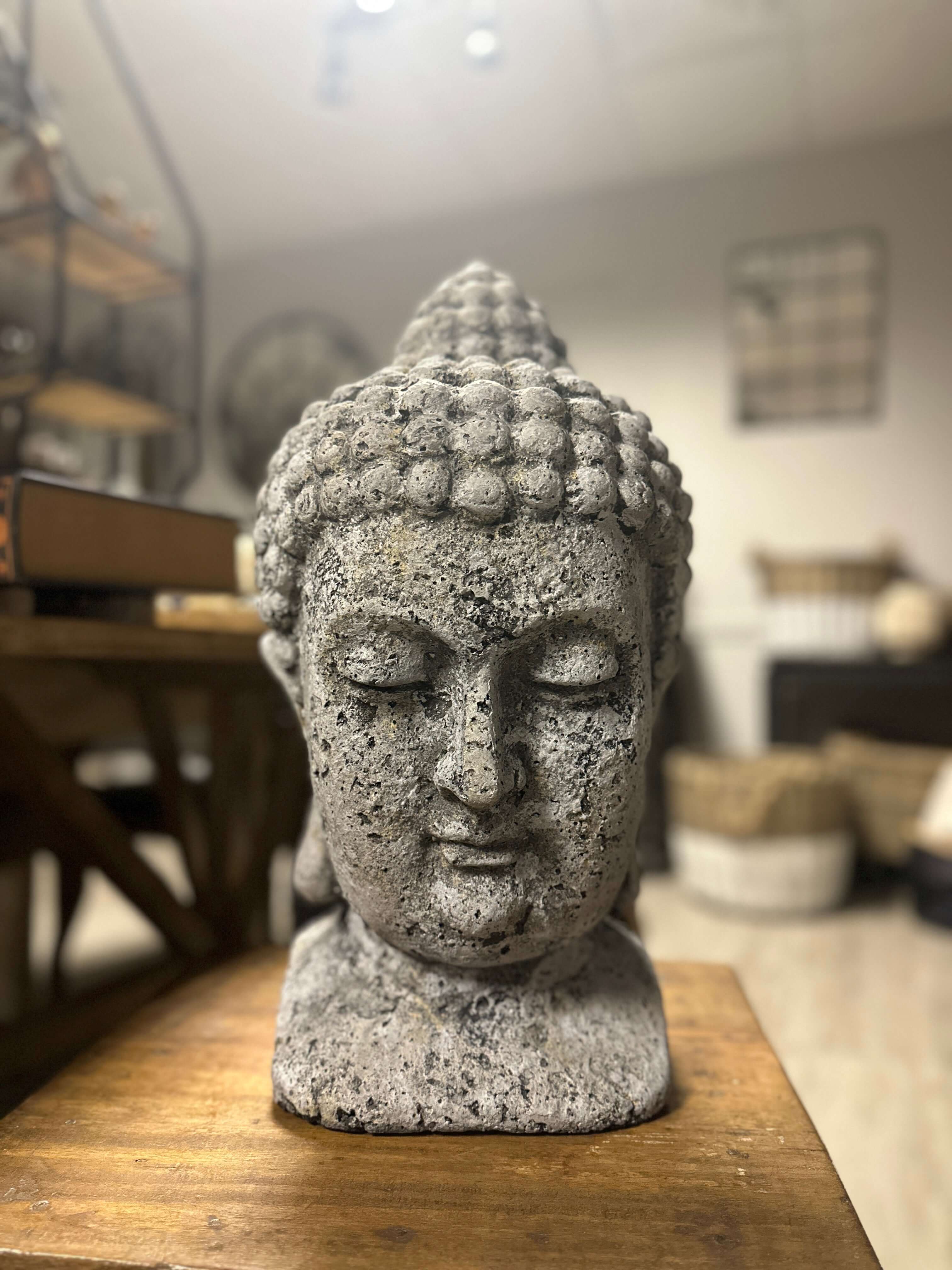 Stone Buddha head sculpture on a wooden surface with a blurred indoor background