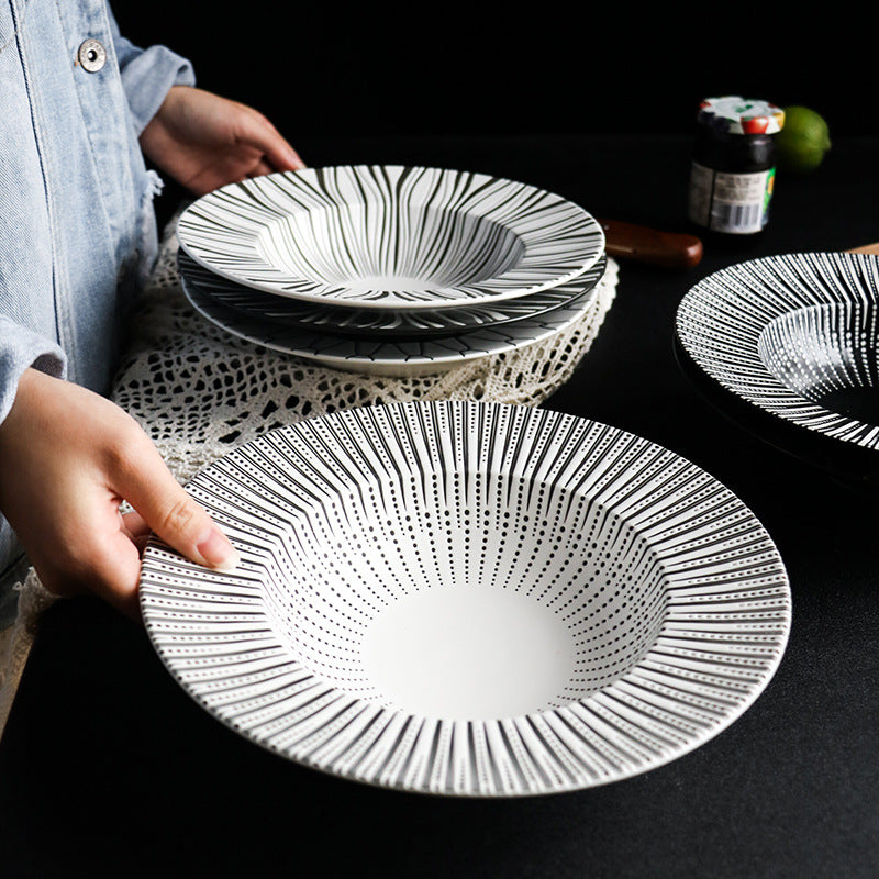 Person holding a black and white patterned ceramic plate on a dark surface.