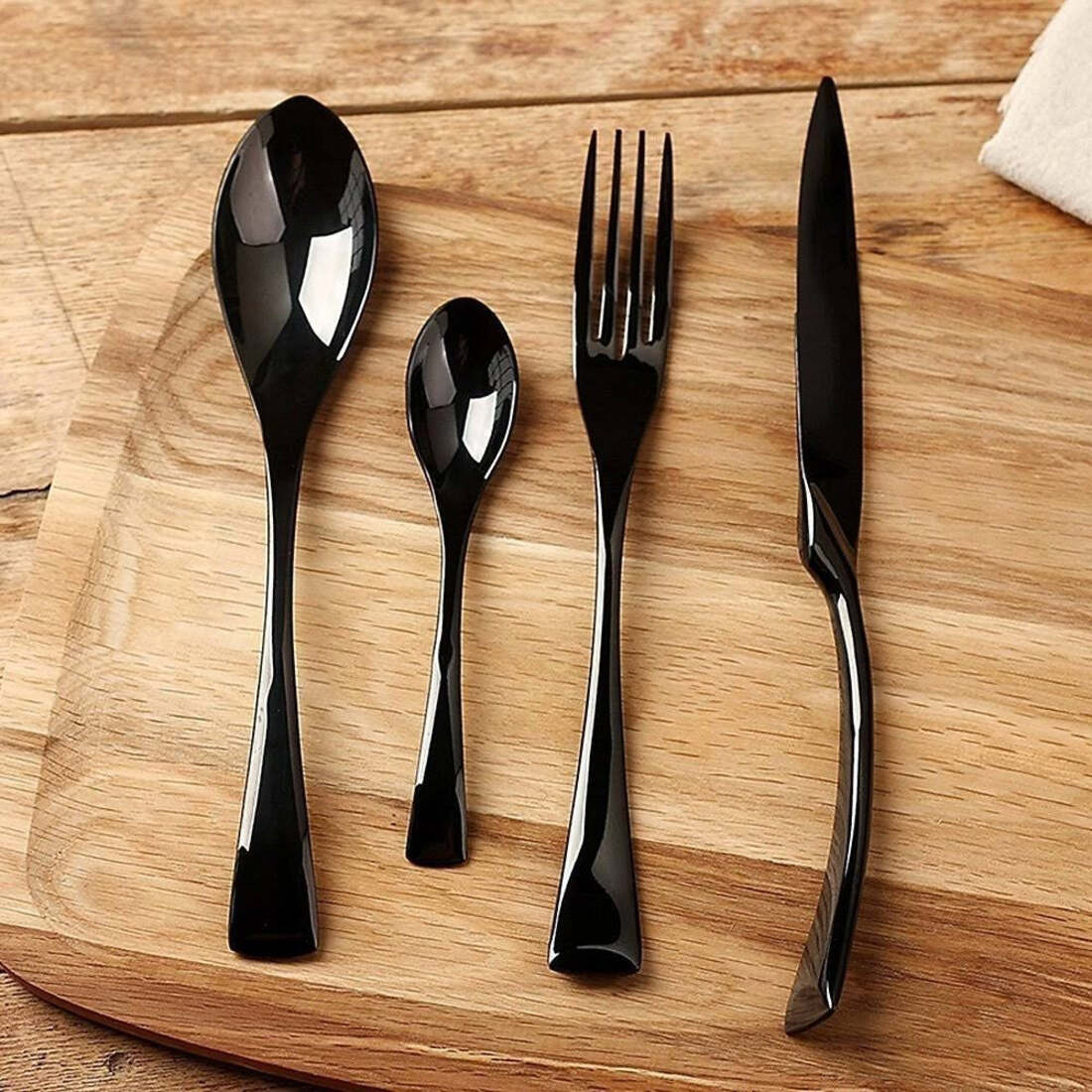Set of black cutlery including a spoon, fork, and knife on a wooden surface.