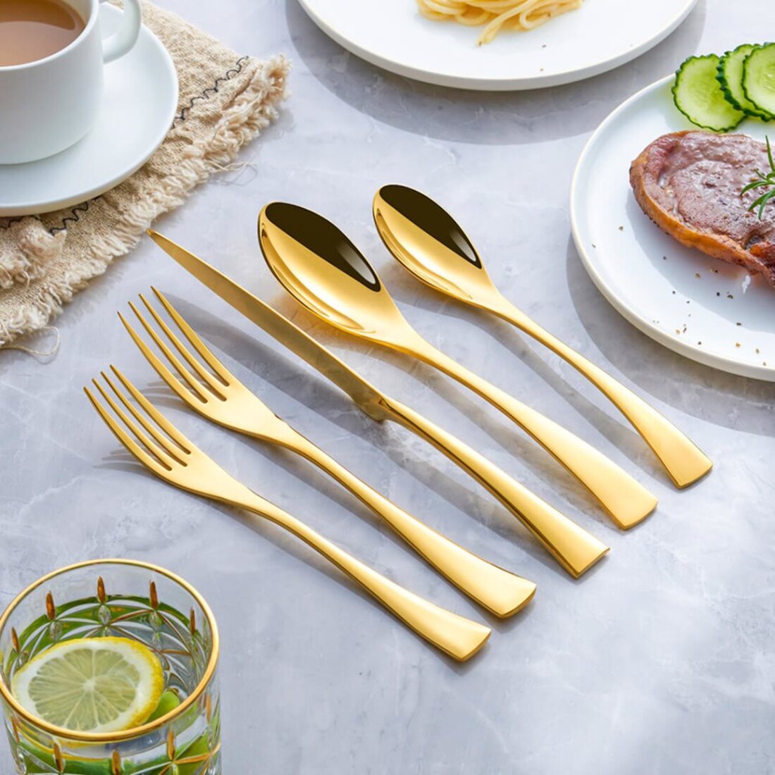 Set of gold cutlery on a table with plates of food and a glass of water.