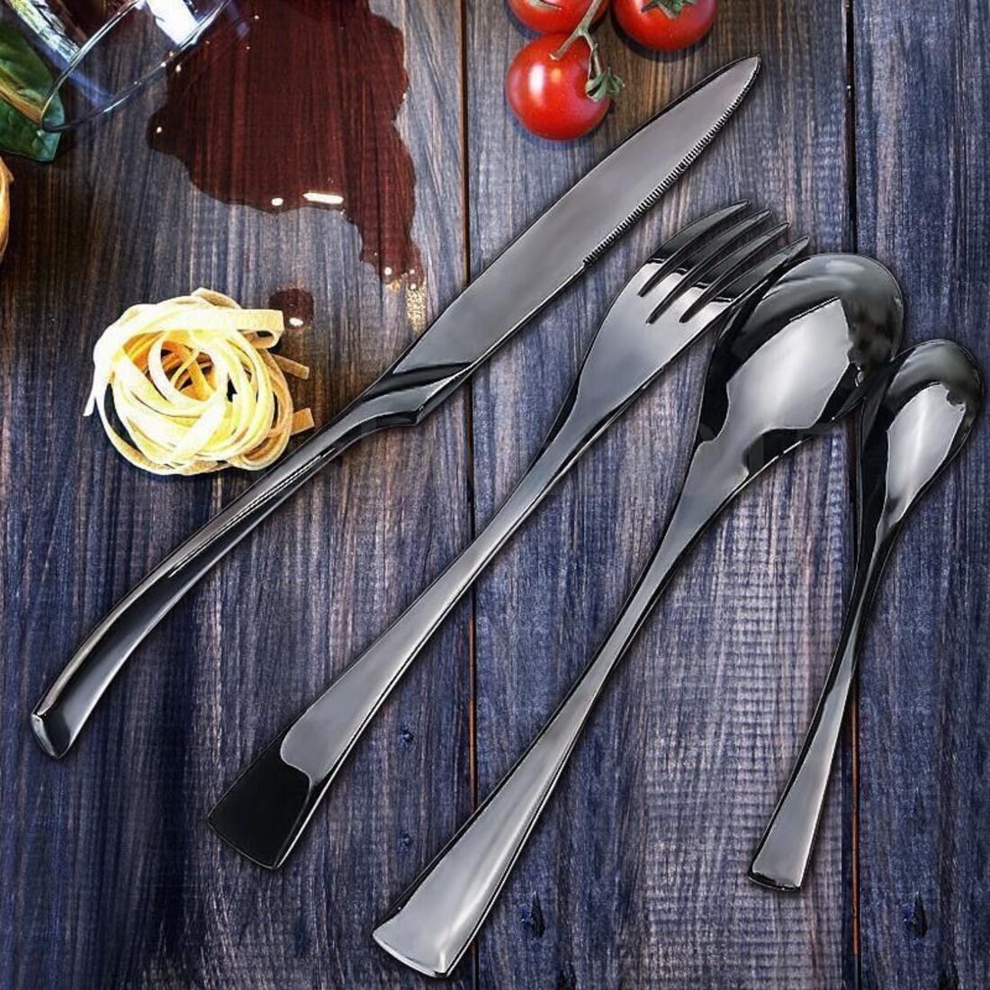 Set of silver cutlery on a wooden surface with tomatoes and pasta.