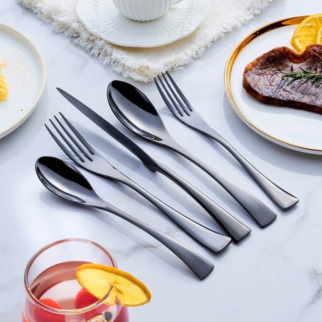 Set of silver cutlery on a table with plates and a glass of juice.