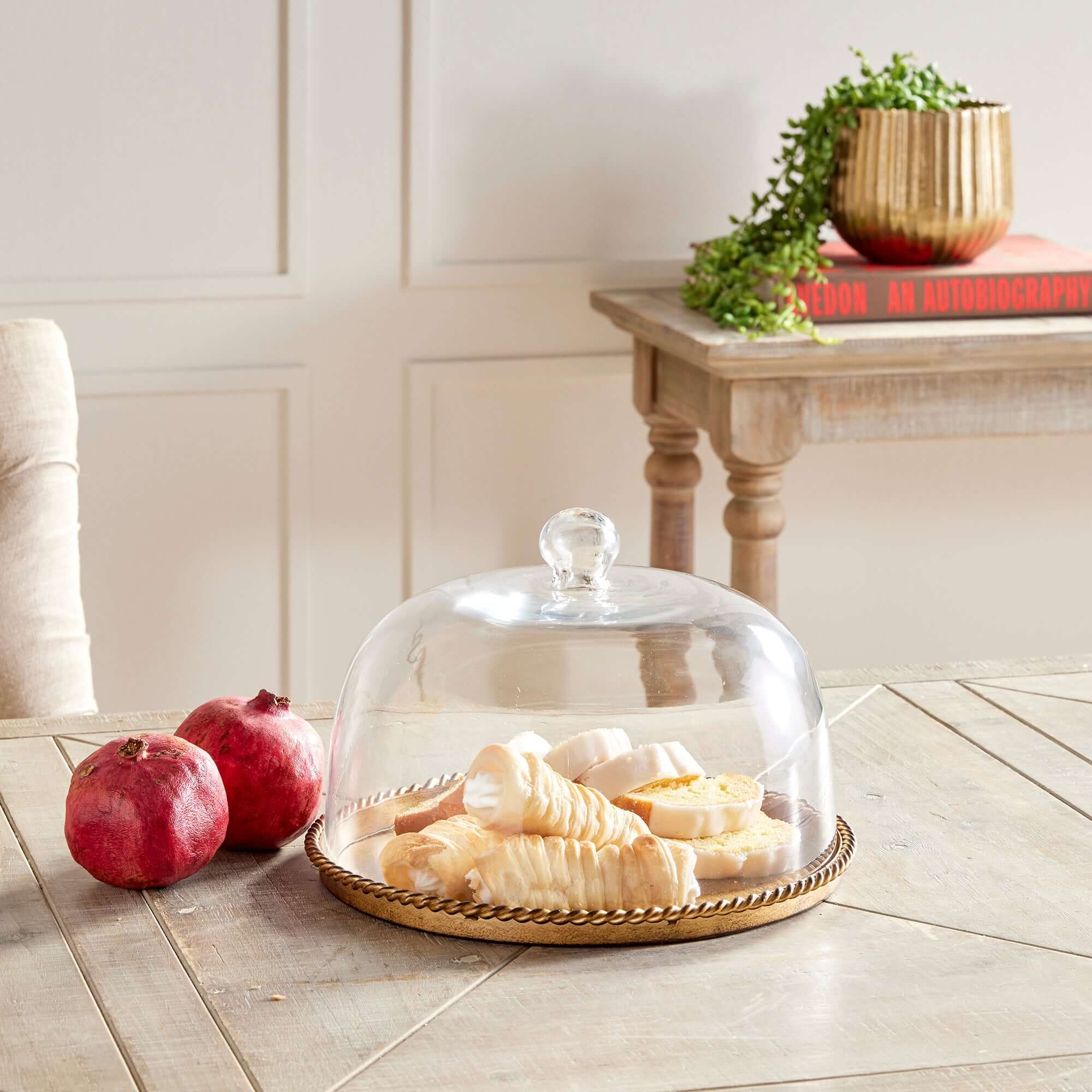Glass cloche with food on a wooden surface next to pomegranates