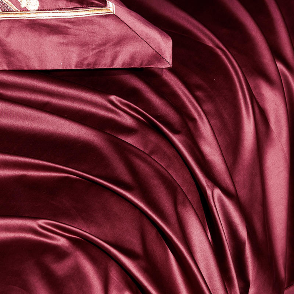 Close-up of maroon satin fabric with a rose gold clutch.