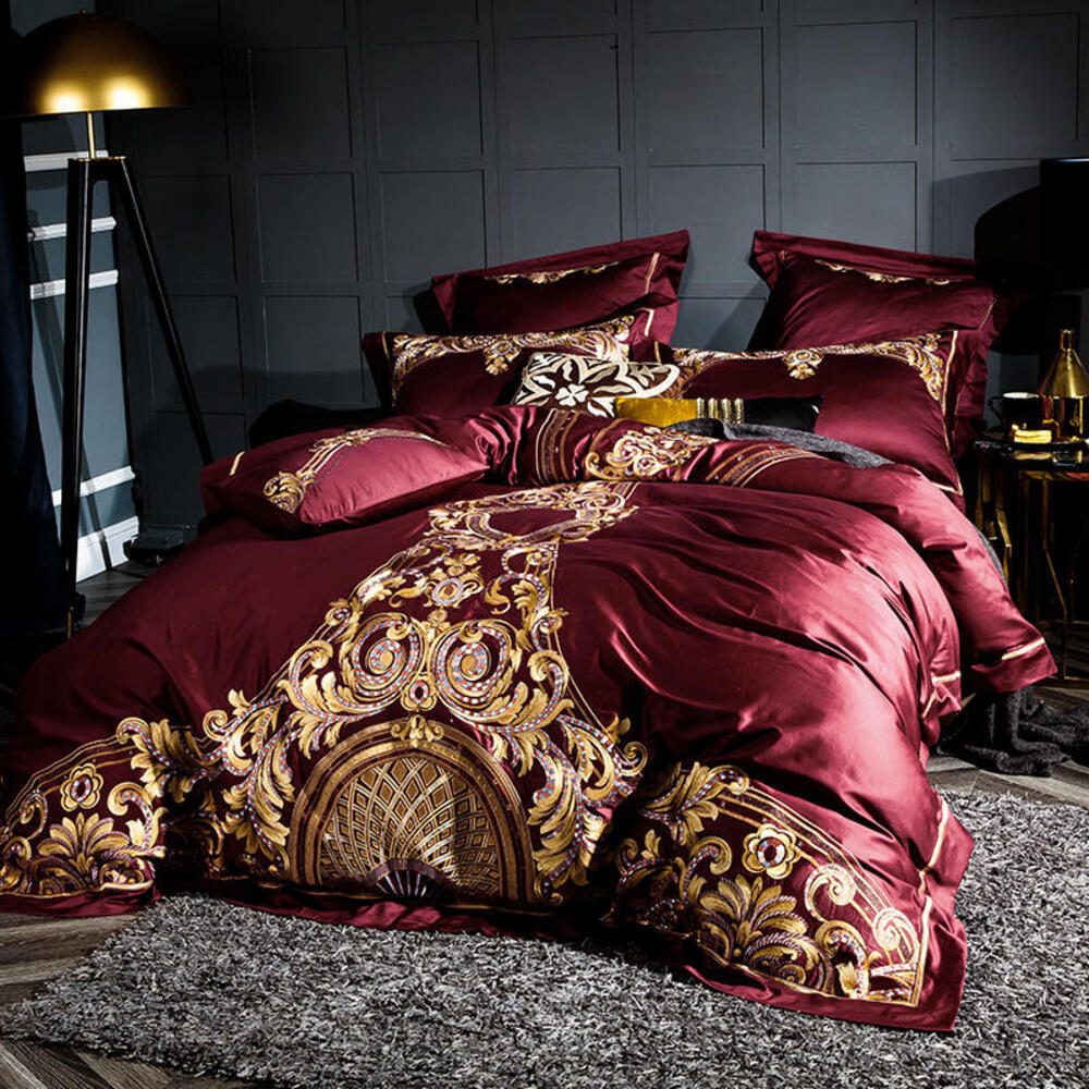 Maroon and gold bedding set on a bed in a darkly decorated room.