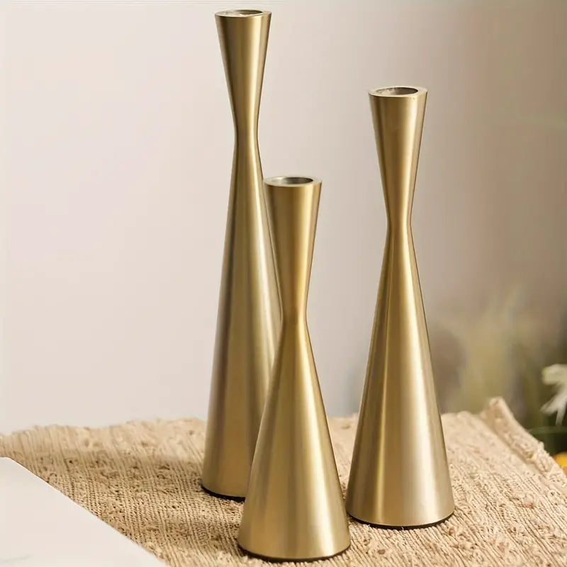 Three gold candle holders in different heights on a textured surface with a blurred background