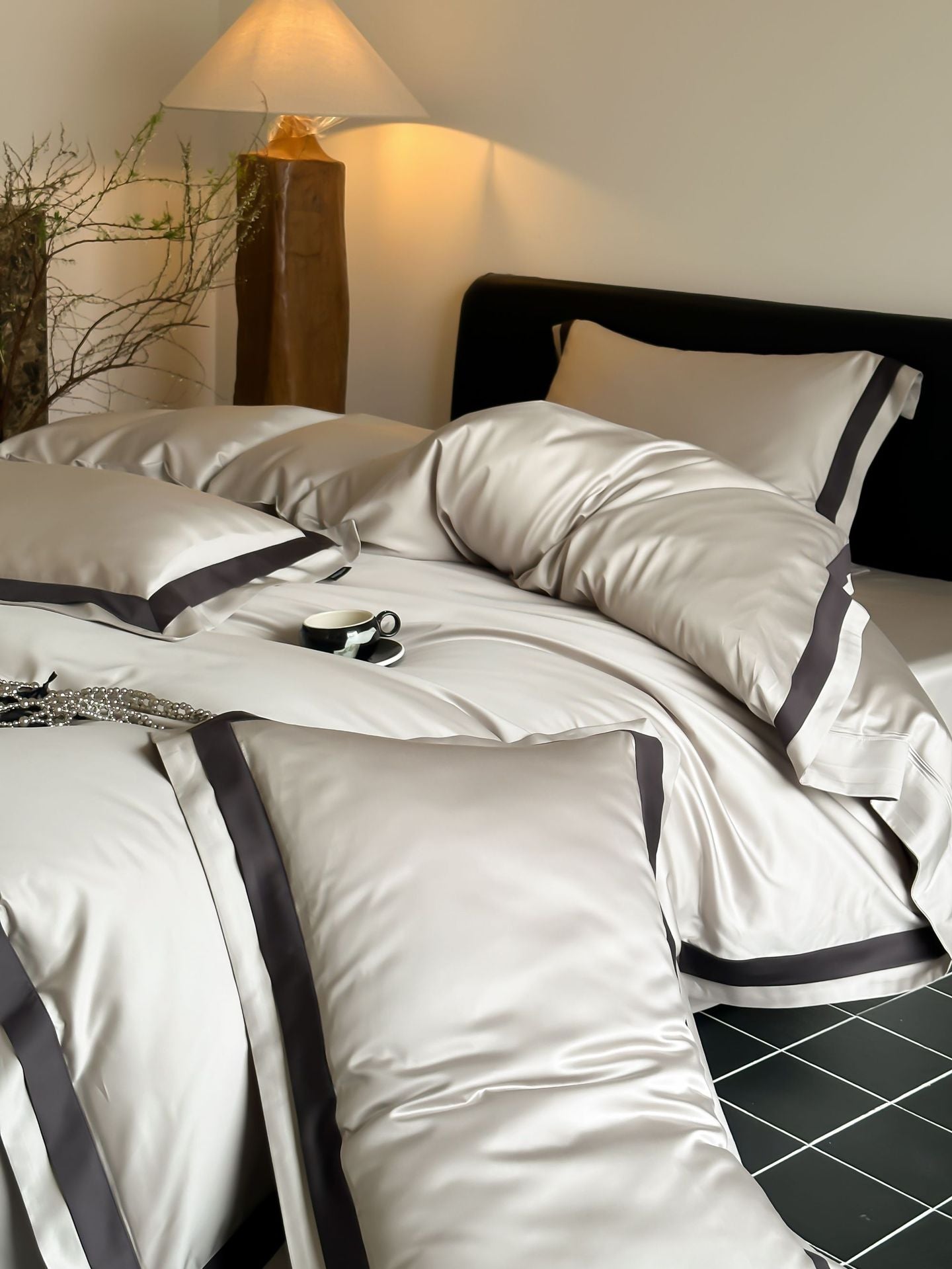 Neatly made bed with white bedding and black trim in a bedroom setting.