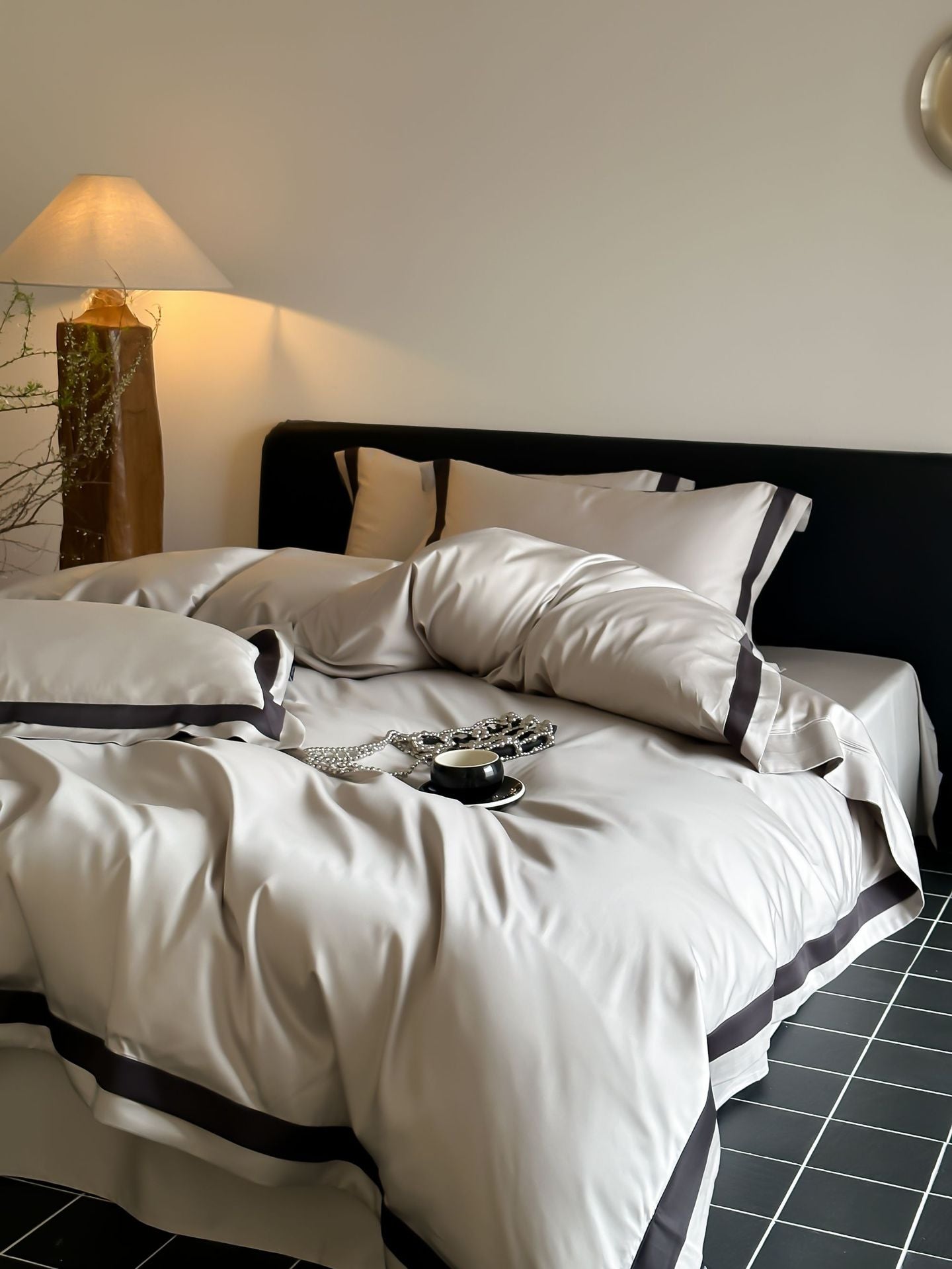 Neatly made bed with white bedding and black trim in a bedroom setting.