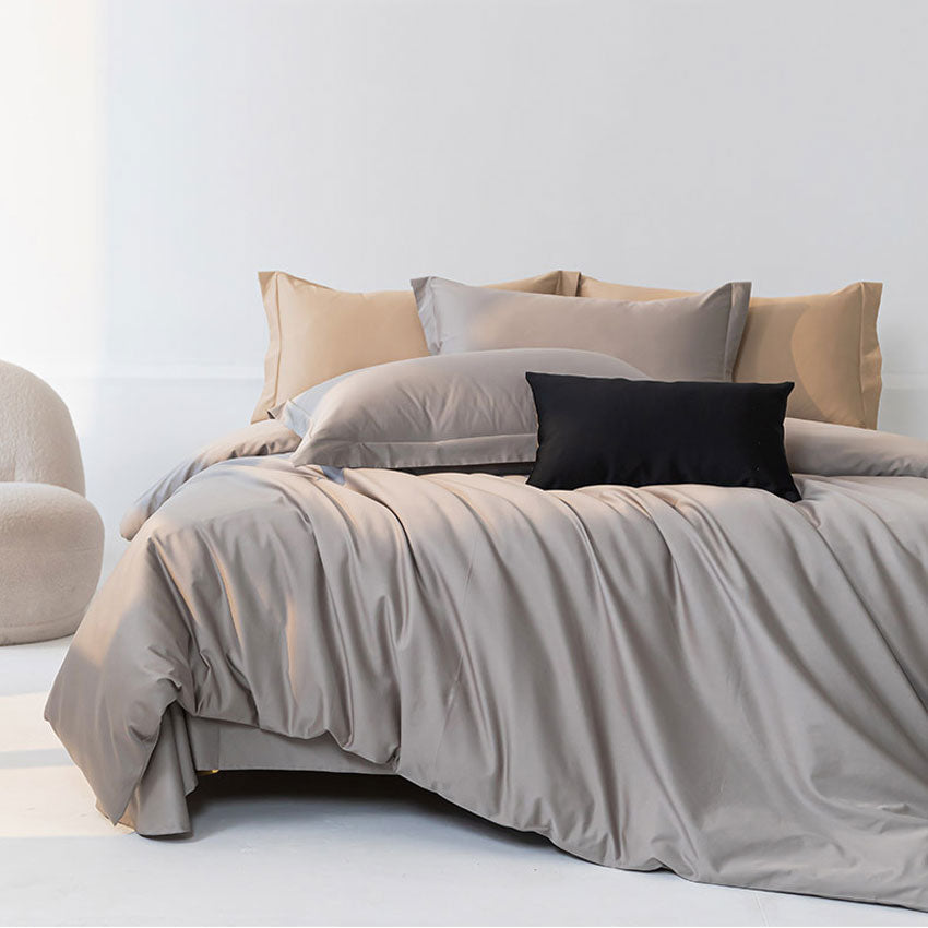 Neatly made bed with beige and gray bedding and pillows in a minimalistic room.