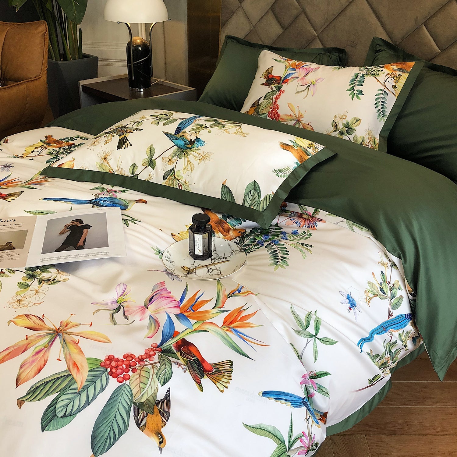 Bed with floral and bird patterned bedding, green pillows, and a lamp in the background.
