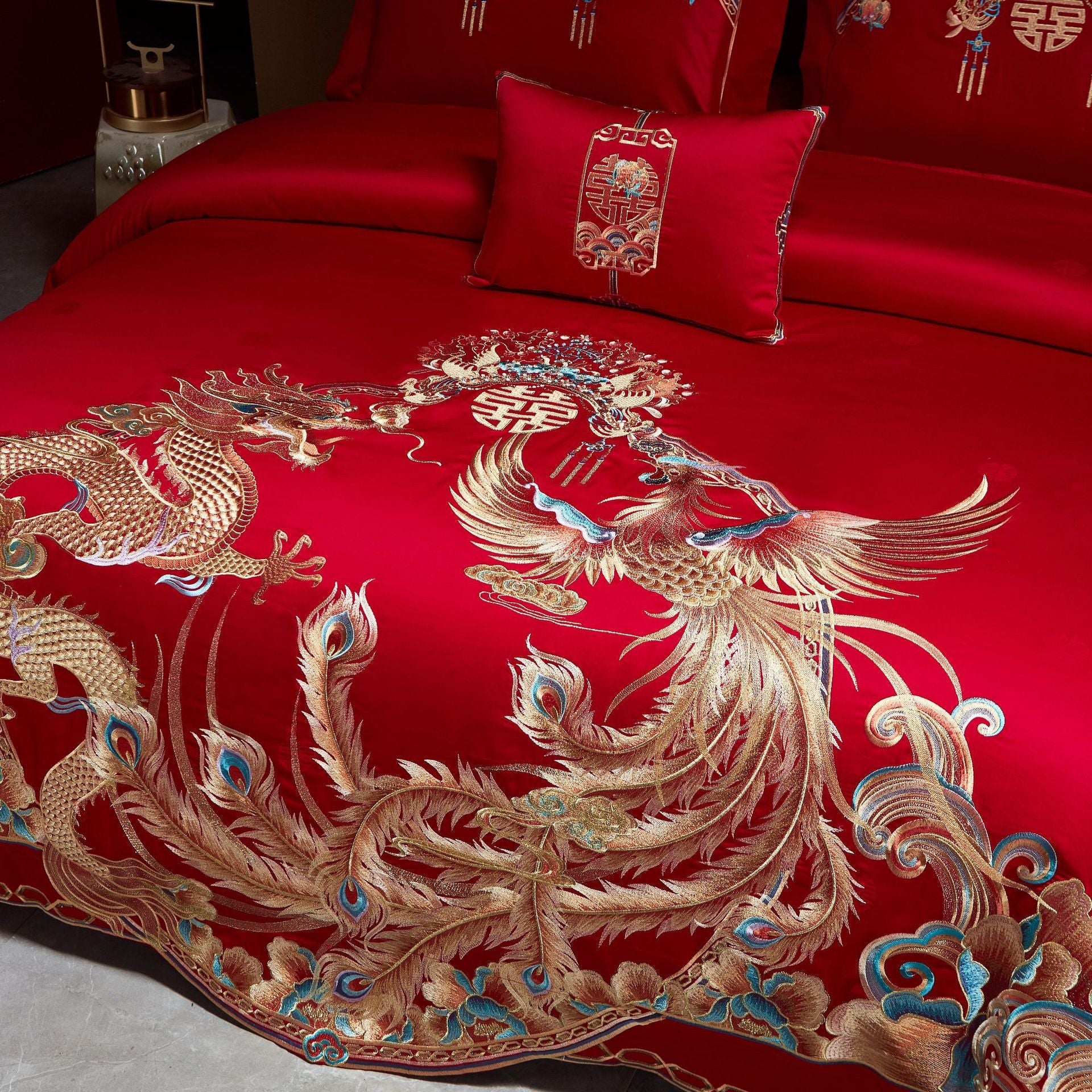 Red embroidered bedding set with dragon and phoenix design on a bed.