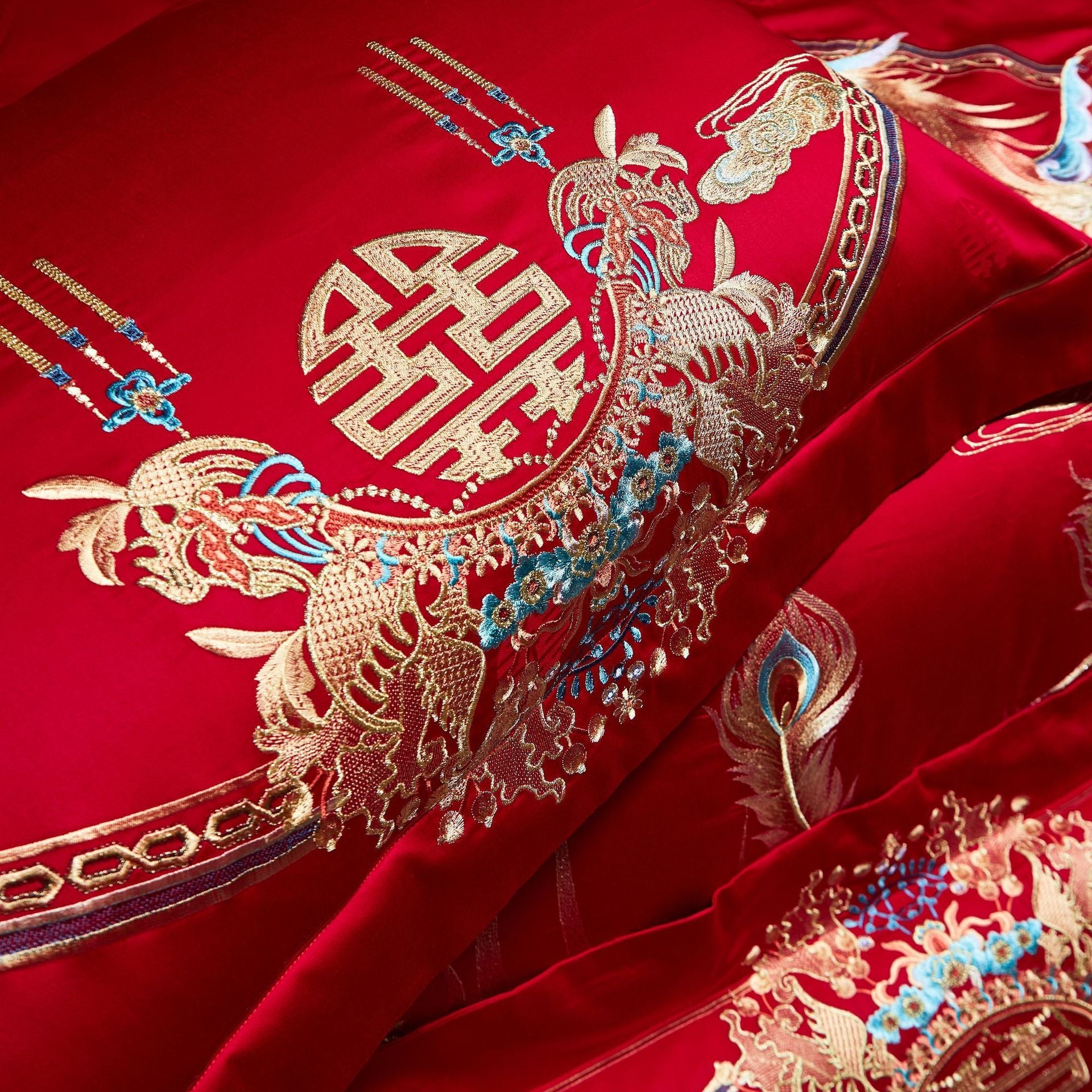 Decorative red fabric with gold and blue embroidery featuring a peacock and Chinese characters on a red background.