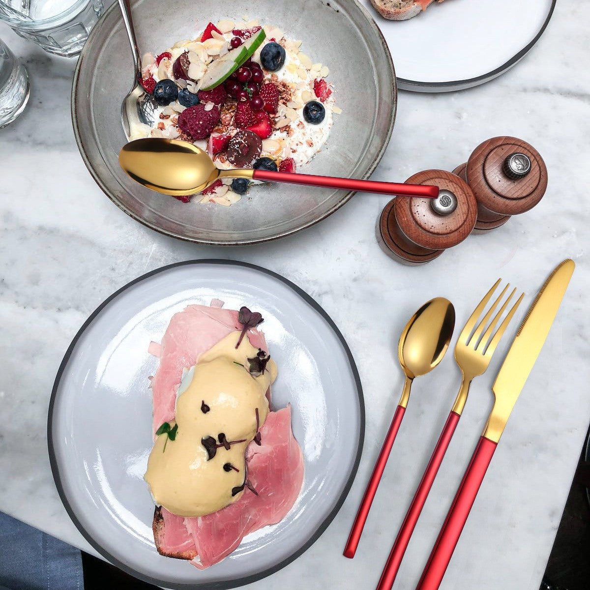 Two plates of dessert with gold and red cutlery on a marble surface