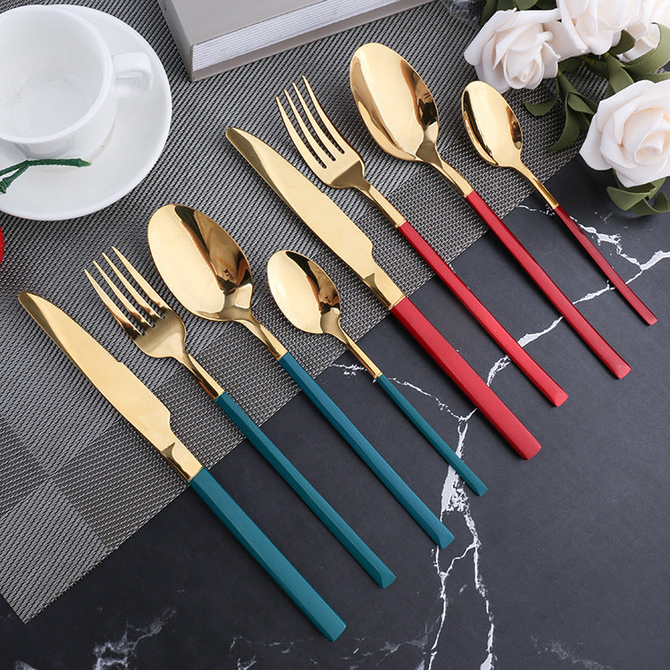 Set of gold cutlery with red and blue handles on a dark surface with flowers.