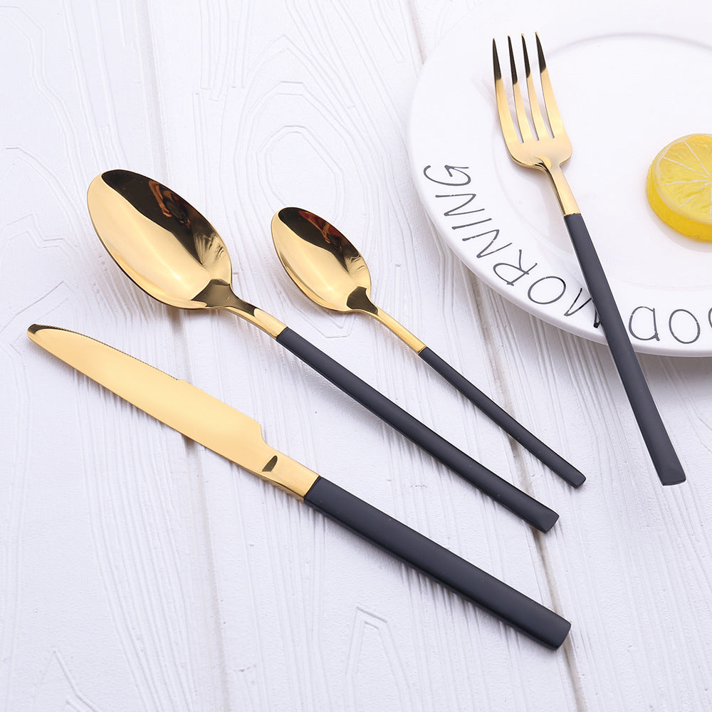 Gold and black cutlery set on a white surface with a plate and lemon slice in the background.