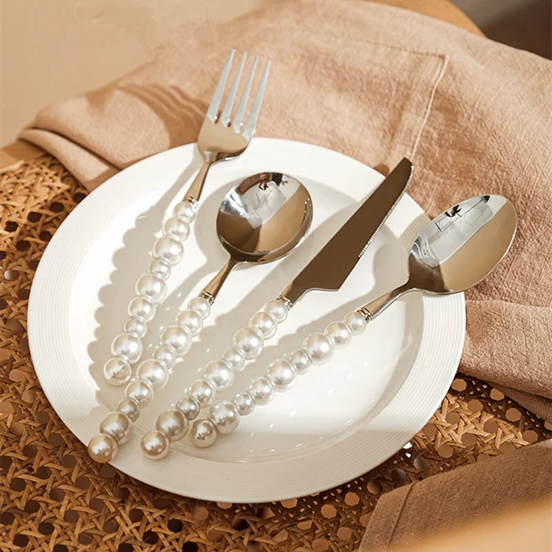 Silver cutlery set with pearl handles on a white plate, placed on a textured surface.